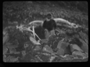 Image of Inuit man by whale ribs among rocks